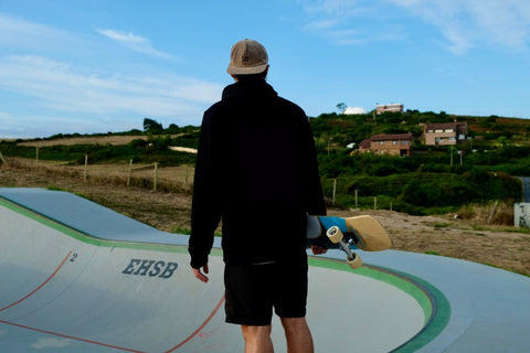 Mann mit Skateboard unter dem Arm steht an einer Skatebowl